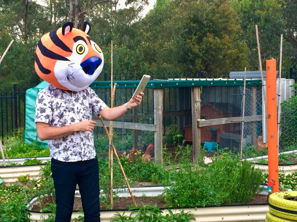 Craig in a tiger mask, holding a tablet in a garden